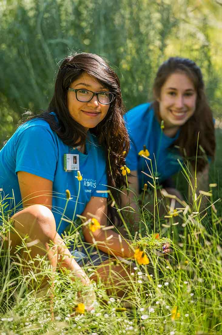 Two teens outside, looking at the camera and smiling. Both are wearing blue t-shirts. 