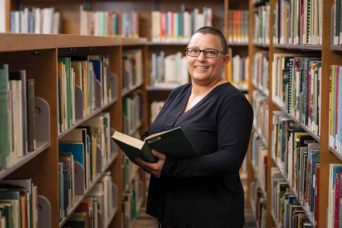 Person in the library smiling and holding open book 