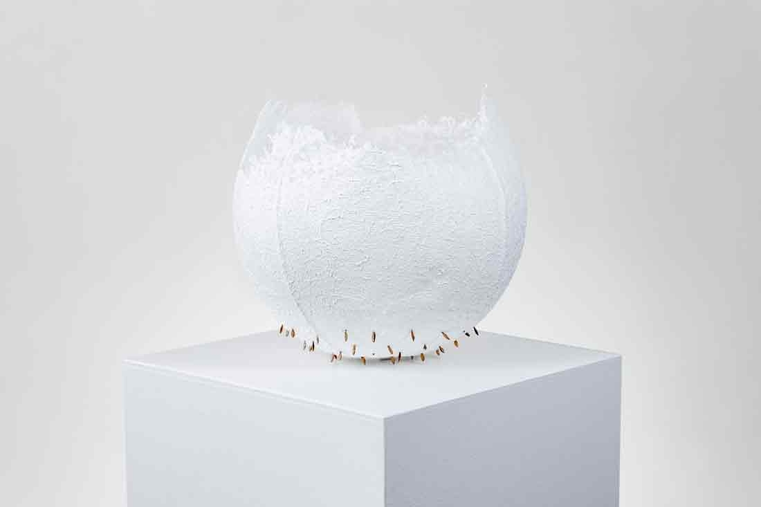 Karen Eberle-Smith, "Exploring Fragility," handmade paper, cheesecloth, wheat spikes and gold paint, 2023. White sculpture with wheat spikes and gold paint sitting on a white pedestal.