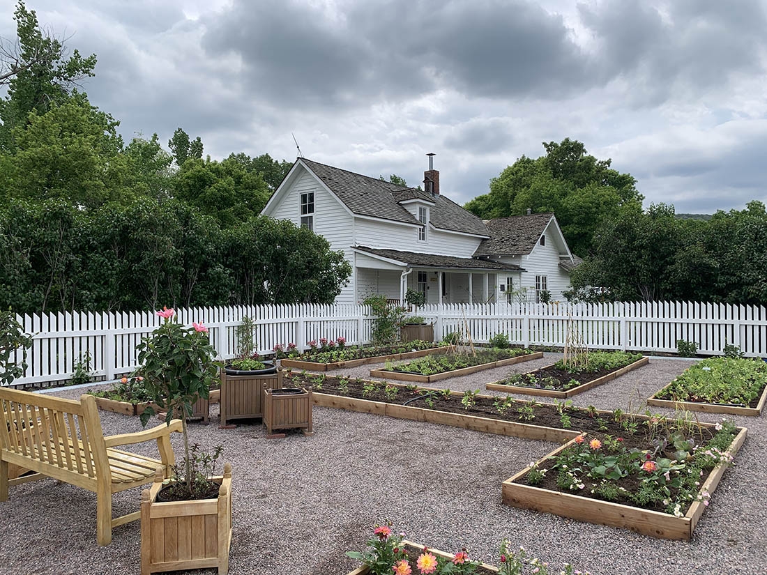 raised garden beds, a wood bench and a white farm house