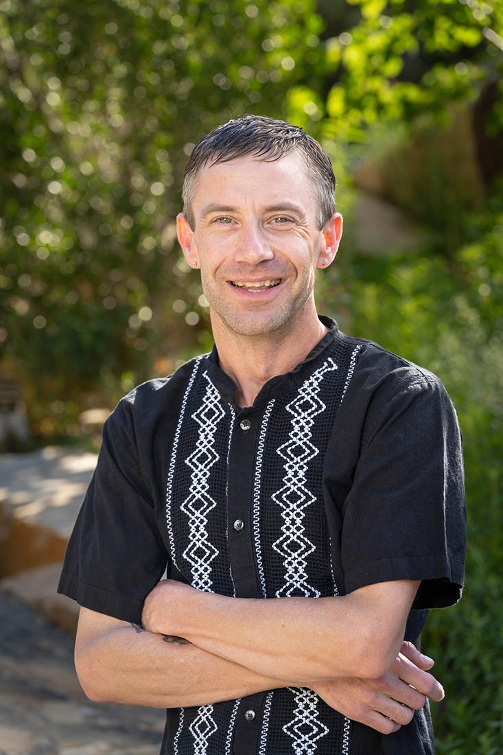 Man in black button-up shirt smiling with arms crossed