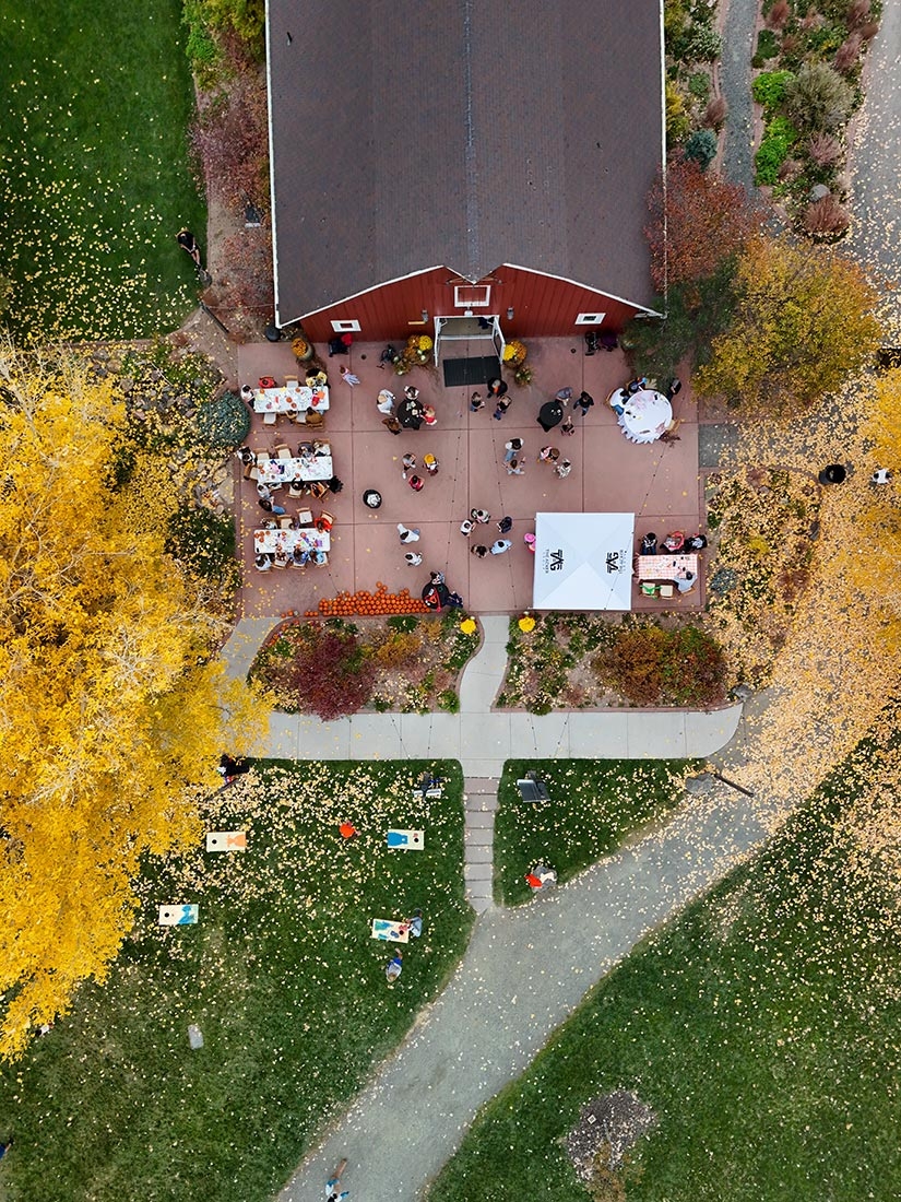 Aerial view of a barn with a patio. Tables and chairs are outside on the patio. 