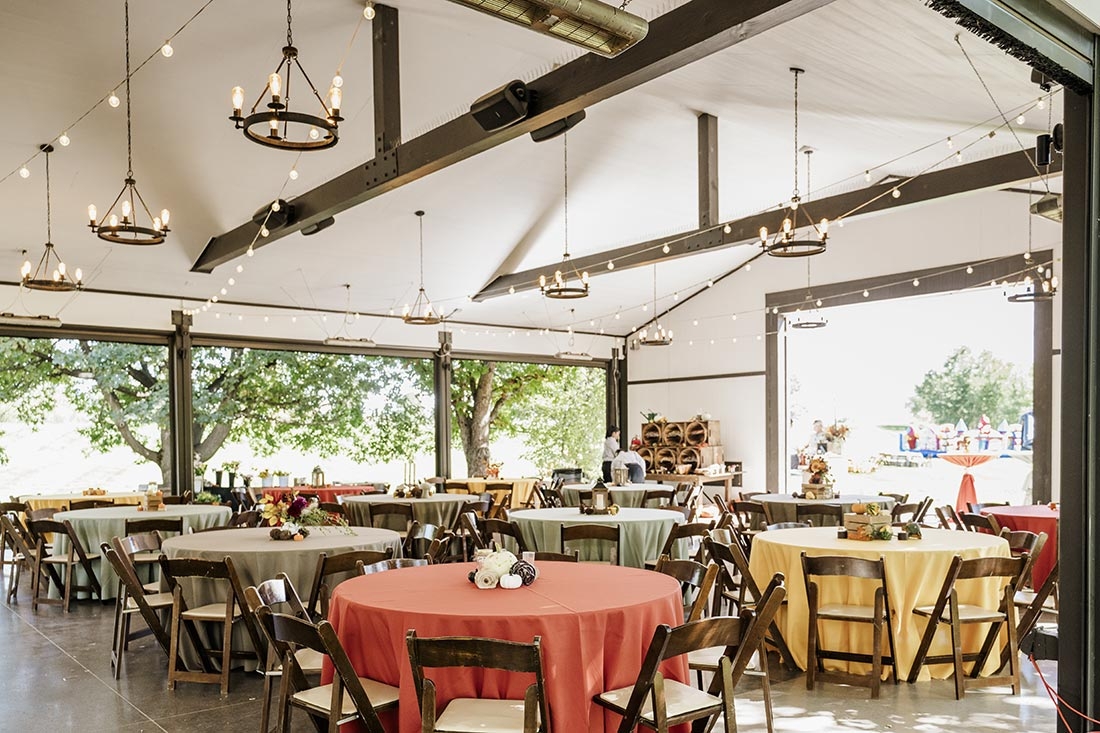 The inside of a building with tables set up for a wedding reception. The walls are open so you can see plants and sunshine. 