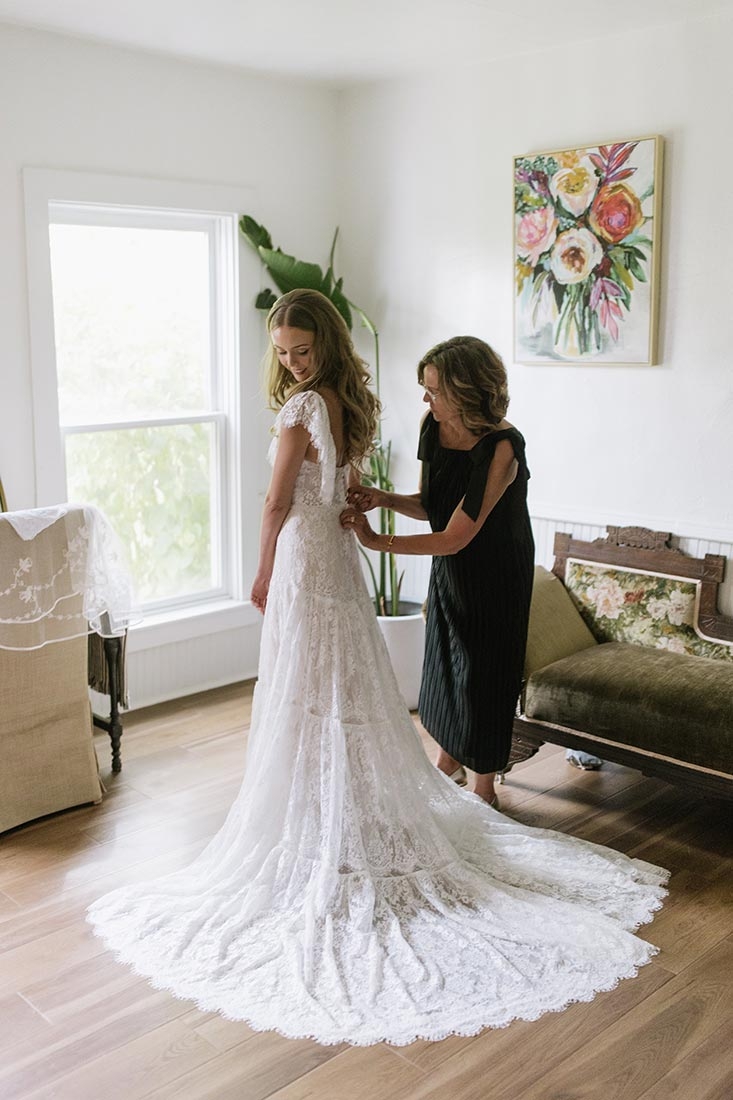 Bride getting ready for her wedding with a person adjusting the back of her wedding dress