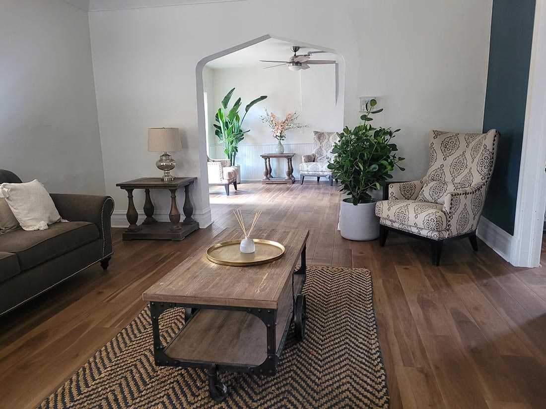 Inside the Polly Steele Center with wood floors, a sofa and chair with a coffee table in the foreground and a sunlit room in the background. 