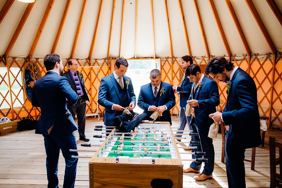 Groom and groomsmen inside a yurt getting ready for a wedding with a foosball table in the foreground