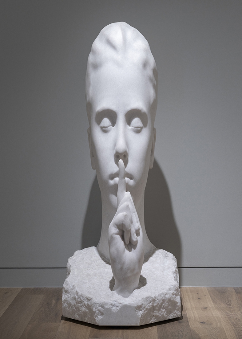 Marble sculpture of person with closed eyes holding a finger up to their mouth.