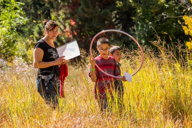 Family Programs Adult and two children out in a high grass prairie field with a hula hoop