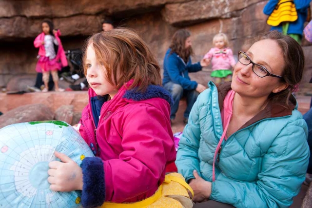 Family Programs Adult in a blue coat and child in a pink coat listening to a story outside. Child is holding a toy globe.