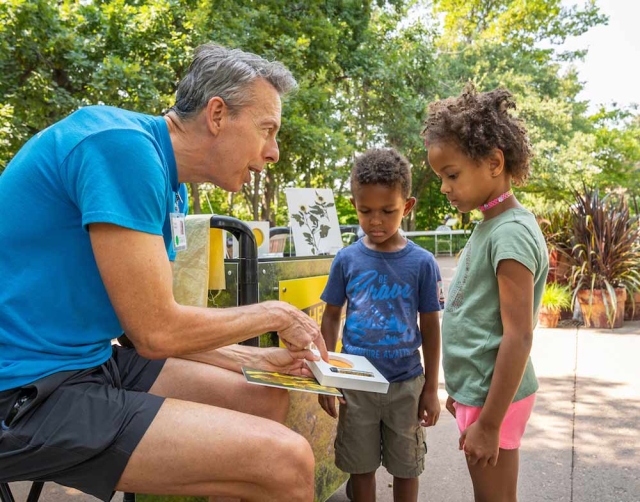 Family Programs Adult in blue shirt showing two children a science project