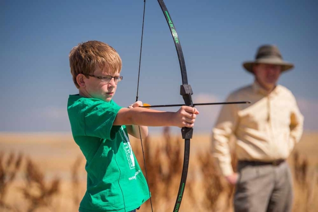 Plains Conservation Center Culd with bow and arrow at Plains Conservation Center with adult in the background.