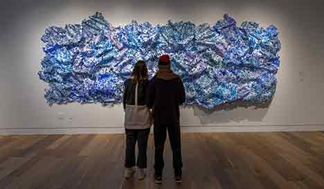 Two people looking at a large blue and pink piece of art hanging on a wall.