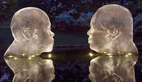 Two sculptures of faces sitting in water and luminated by lights