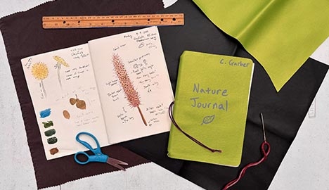 Open Nature Journal notebook with drawings in it, surrounded by scissors, a ruler and a needle with yarn.