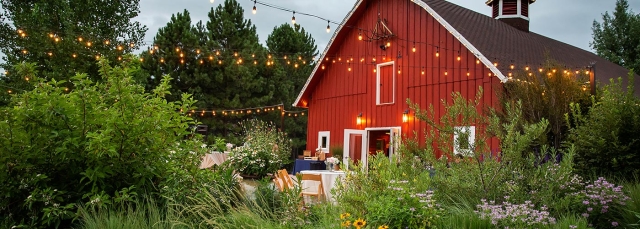 Red barn at dusk with twinkling lights shining on bushes and trees