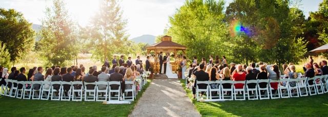 A wedding being held at sunset in a garden with a pergola. Guests are seated facing the pergola