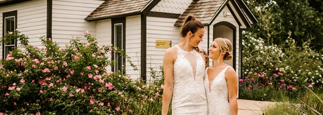 Two people at their wedding looking at each other and smiling in front of an historical schoolhouse