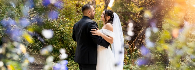Smiling bride and groom outside facing each other with trees in the background