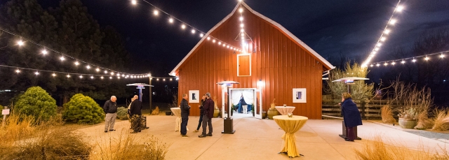 Red barn at night with twinkle lights and people standing at high top tables 
