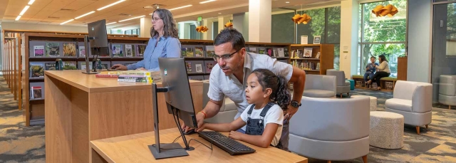 Two adults and a child using the electronic resources in the Helen Fowler Library.