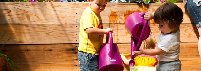 Two toddlers pouring water from watering cans in the Mordecai Children's Garden.