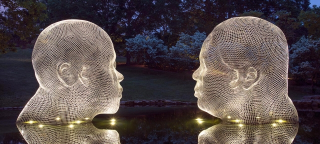 Two steel mesh sculptures of heads in a pond, lit from below.